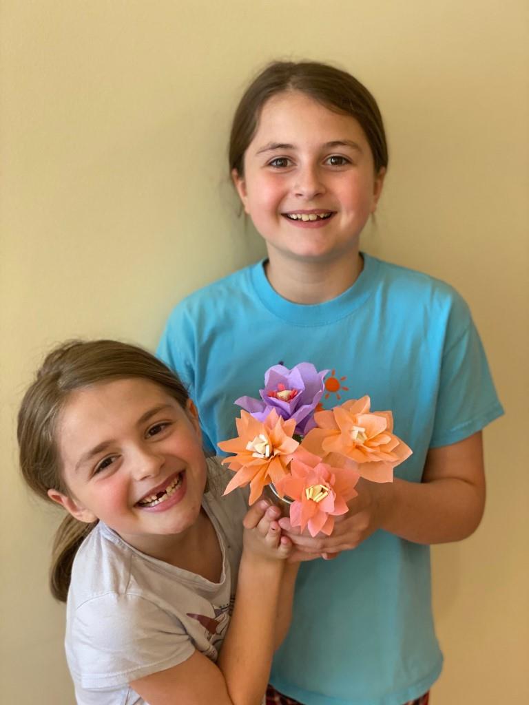 Two young girls smiling and holding a bouquet of fake orange flowers
