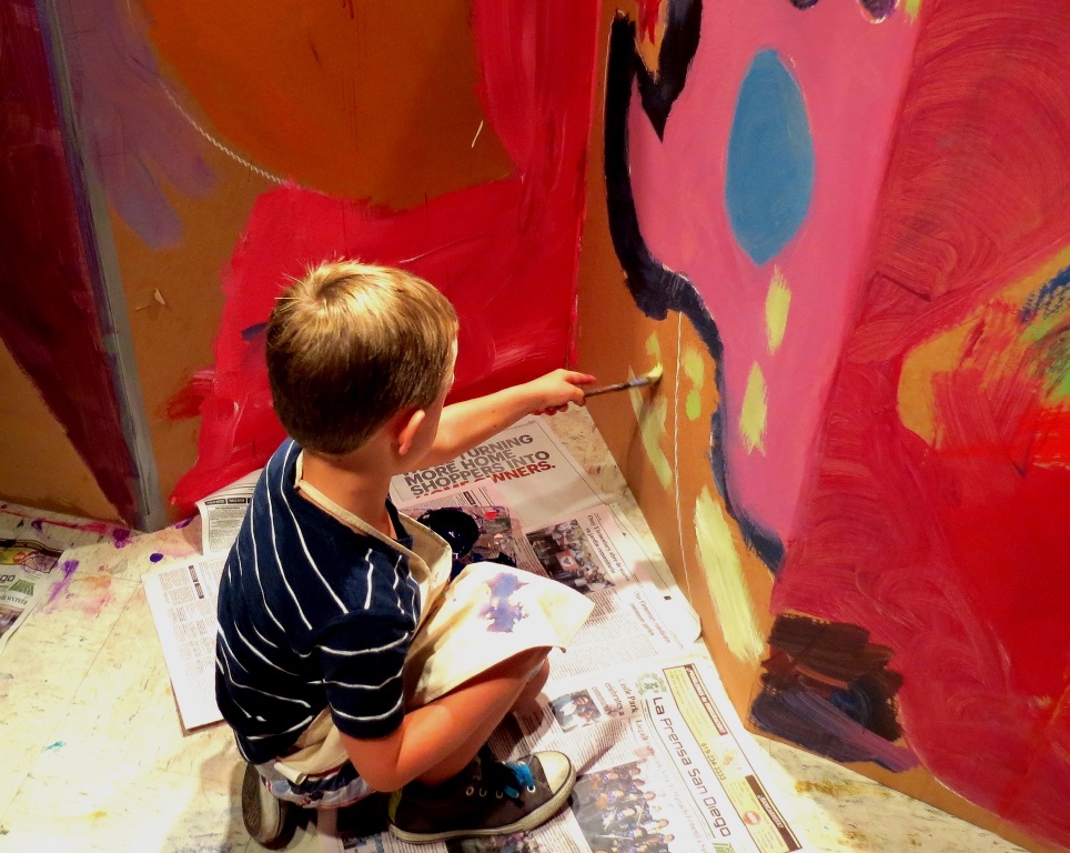 boy painting large wall of cardboard