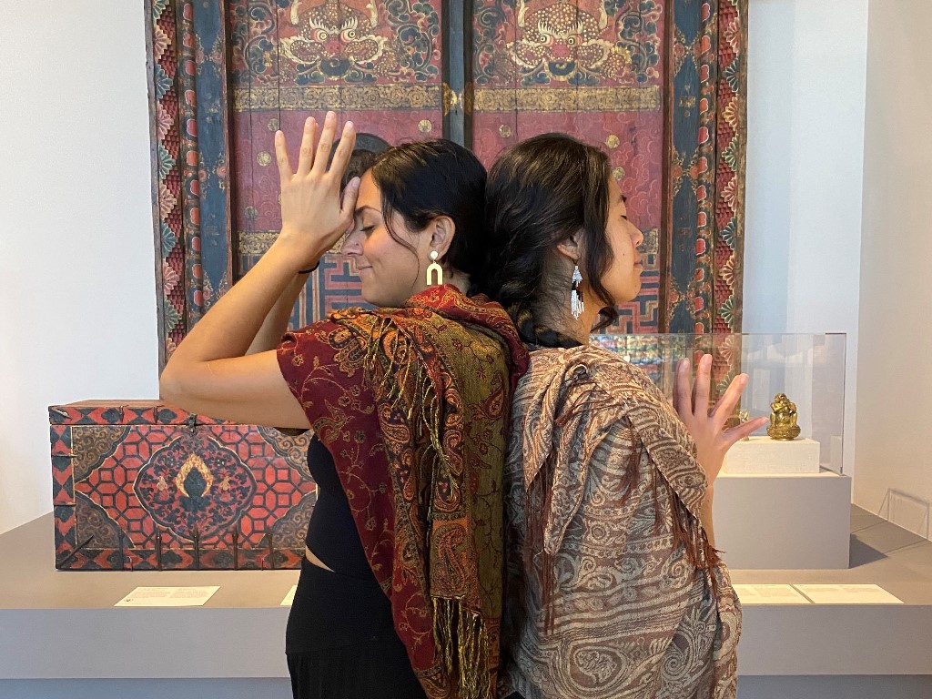 Two women standing back to back meditating in front of Tibetan doors in museum gallery