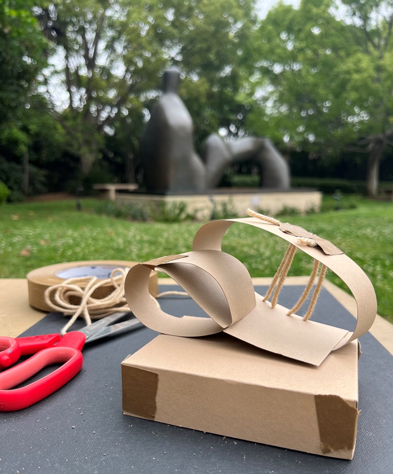 Paper sculpture on table in front of Henry Moore sculpture in museum sculpture garden