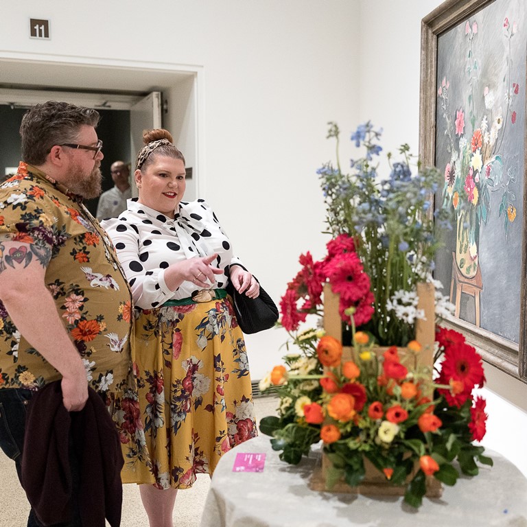 Man and woman looking at floral arrangement and art at Art Alive at The San Diego Museum of Art