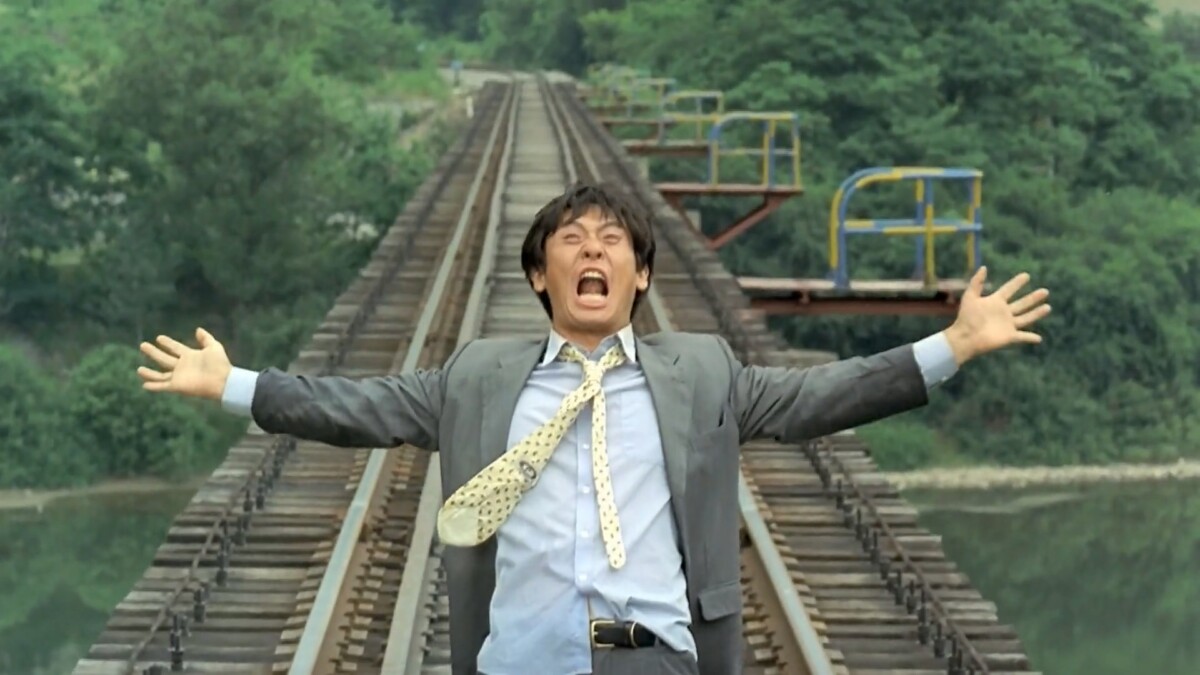 Man with arms wide yellow while standing on empty train tracks