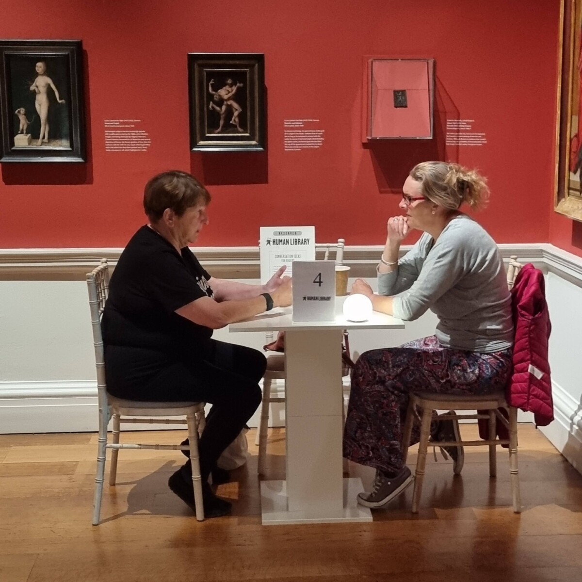 Two people talking at table inside art gallery