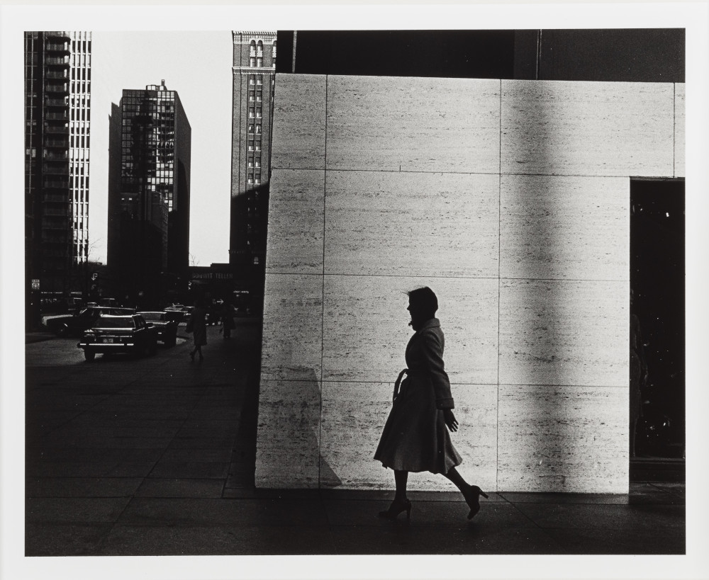 Black and white photograph of woman in trench coat walking