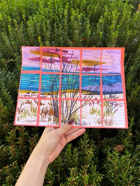 Colored grid landscape held in hand in front of green bush
