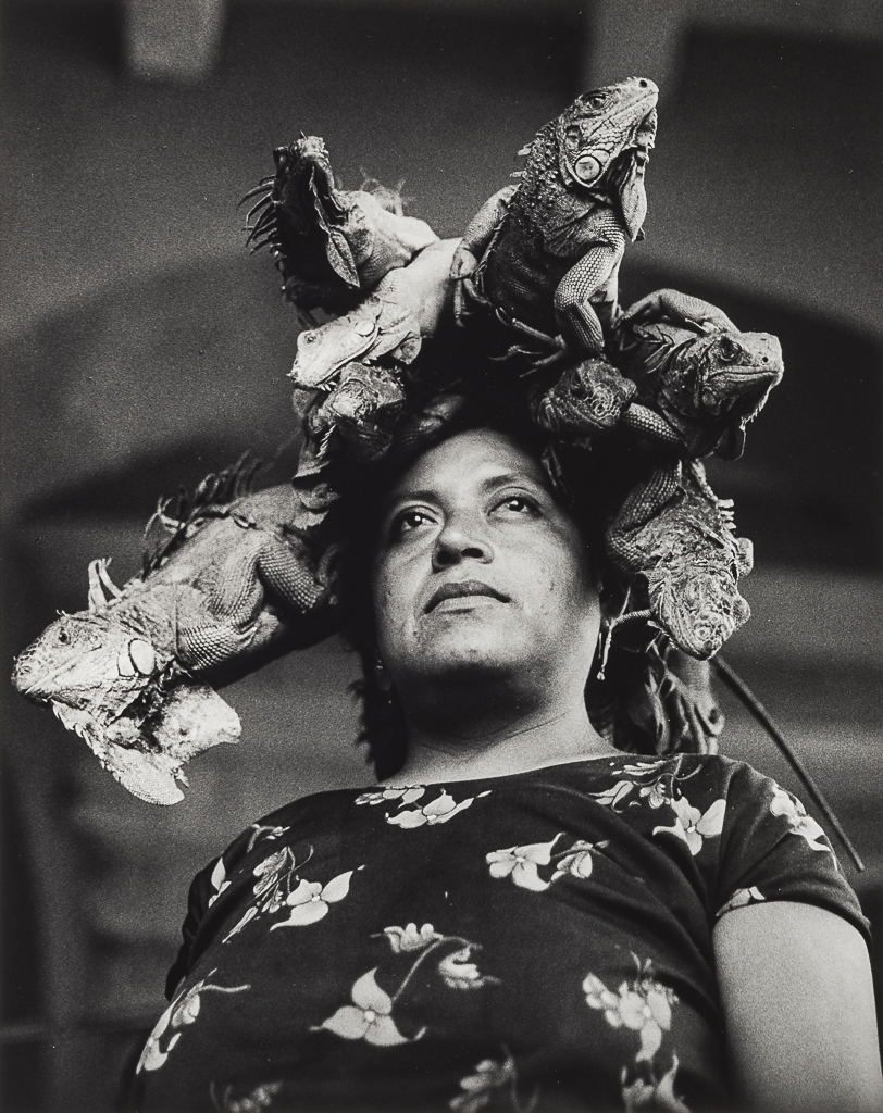 Black and white photograph of women stoically standing with iguanas on her head