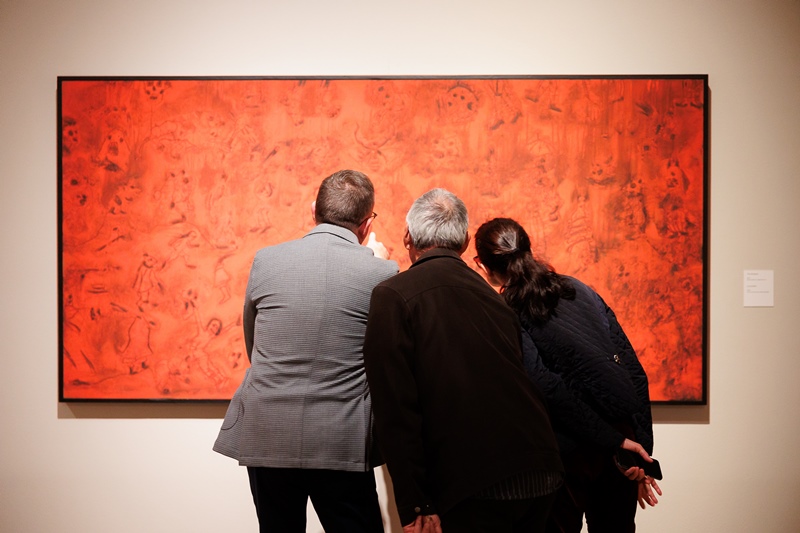 People huddled together looking at large red painting
