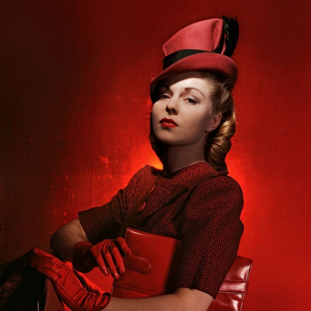 Blonde woman in red dress with red hat and gloves against red background