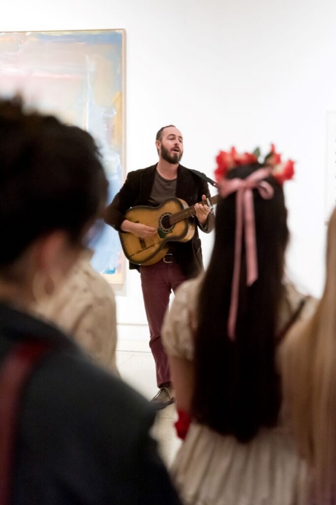Crowd listening to man with guitar in art gallery