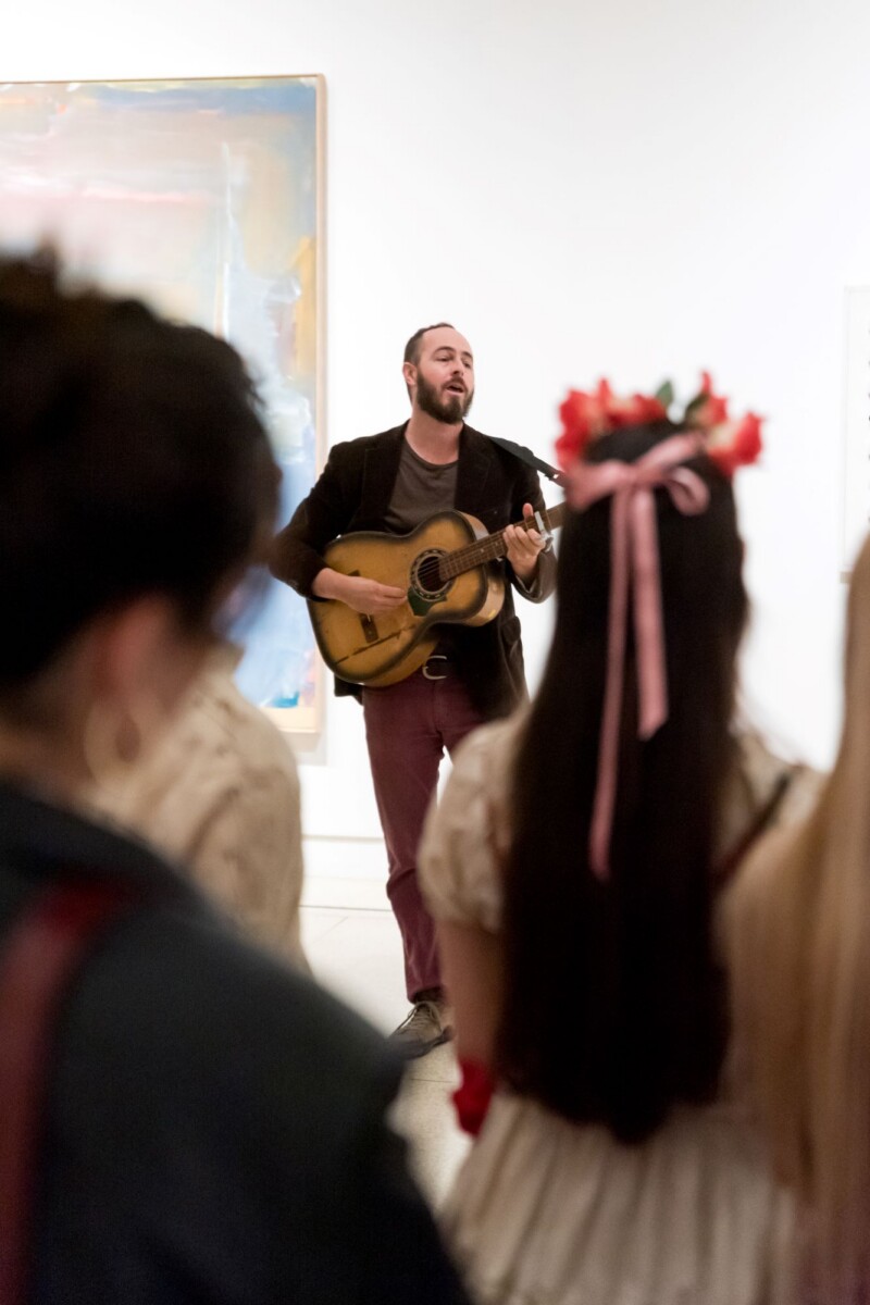 Crowd listening to man with guitar in art gallery