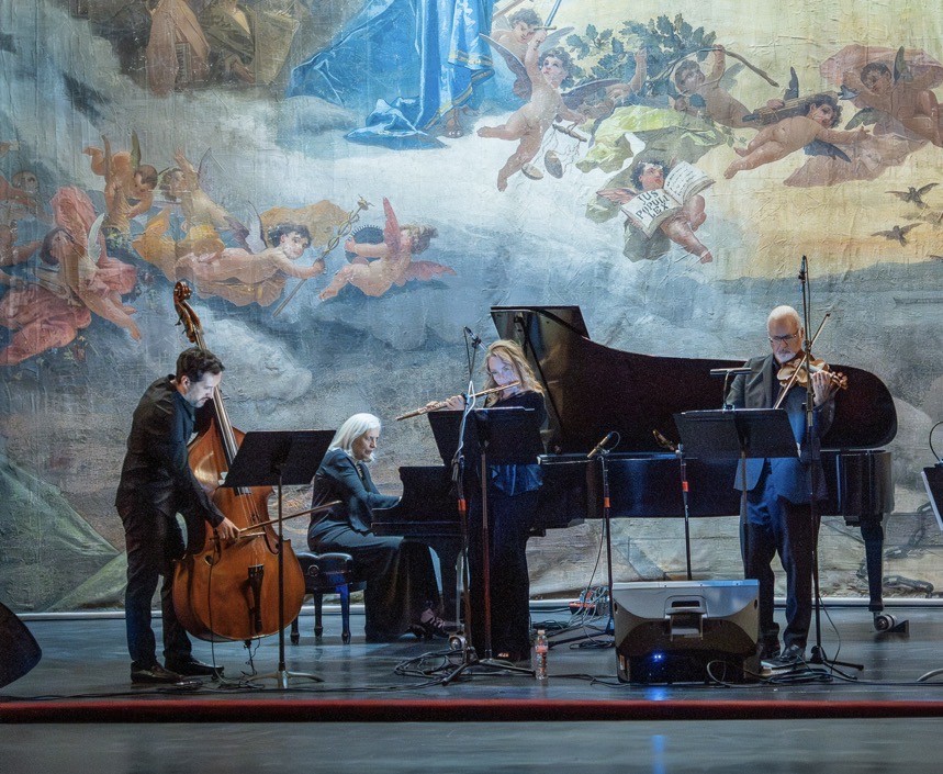 Four musicians performing on stage with tapestry background