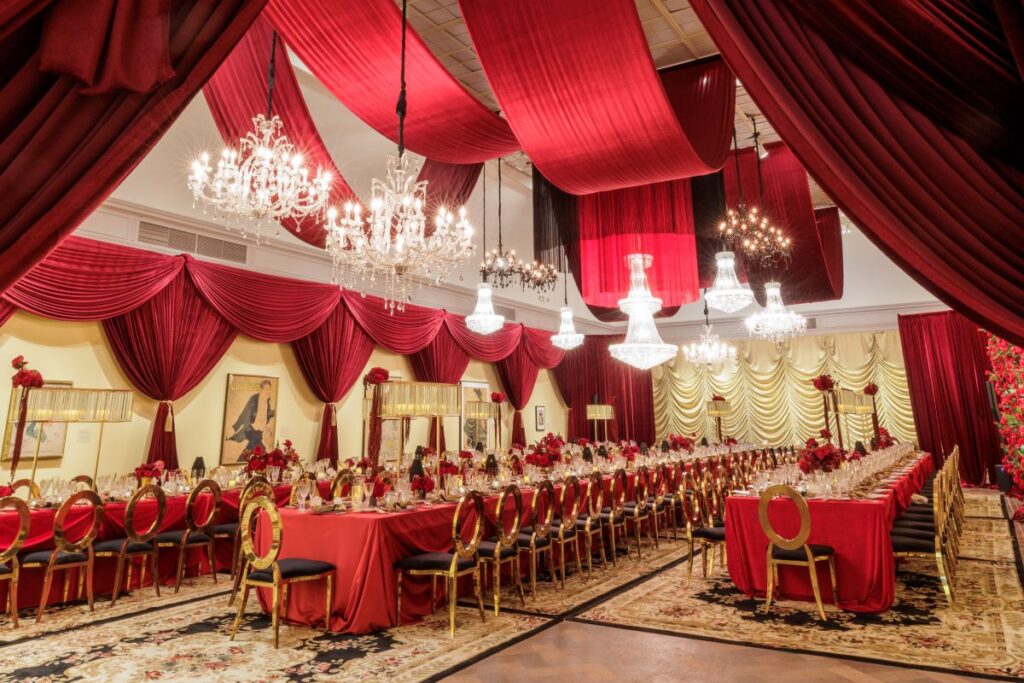 Long tables with red linens in art museum gallery with red draping and chandeliers