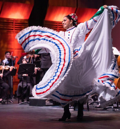 Ballet folklorico dancer performing on stage with orchestra in background